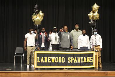 From left, Cortez McKenzie, Derrveron Maxwell-Black, Jalen Stubbs, Coach Cory Moore, Davion Cummings, Derreyon Maxwell-Black and Artez Hooker stand on stage on Feb. 3 in the Lakewood auditorium. Five Lakewood players signed to play football for colleges around the country.