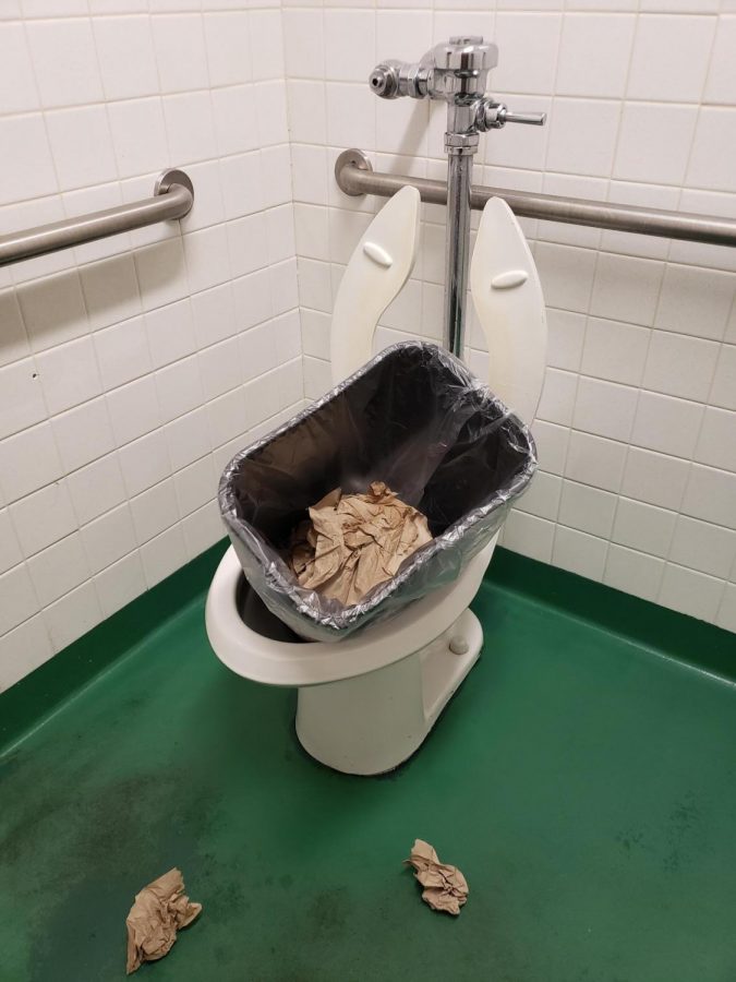 A trash can sits in the toilet of a staff bathroom. 
