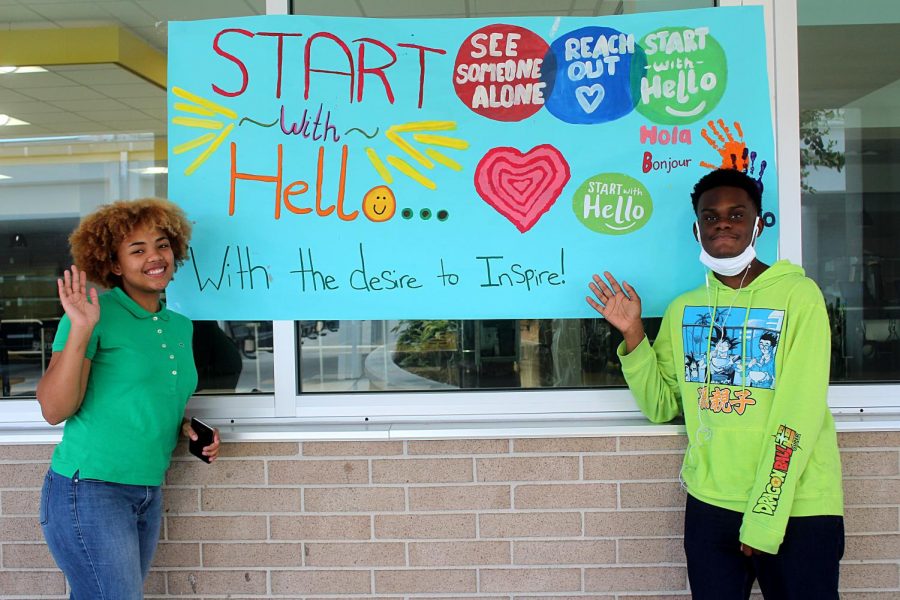 Junior Falicity Ozuna and senior Cameron Copeland pose in front of the Start with Hello week poster on Sept. 22 in front of the cafeteria. The poster was created by the SAVE Club, which organized the week of activities. 