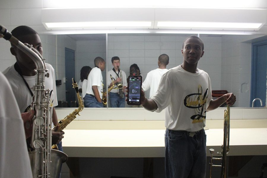 Senior Isaiah Davis holds up a phone with a tuning app as other members  tune themselves to prepare for their performance on Aug. 25.