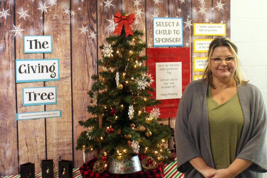 National Honor Society sponsor Heather Robinson poses with the giving tree. The giving Christmas tree is a tree about giving presents to the kids who can’t get one on Christmas day. Heather Robinson is the one who came up with the idea “It’s a great way is to give back to the community,” Robinson said.