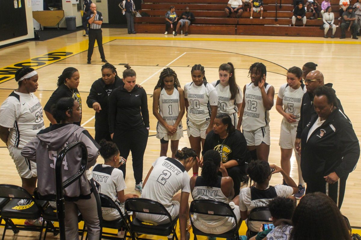 Girls basketball team huddle around to speak to coach Necole Tunsil during game.