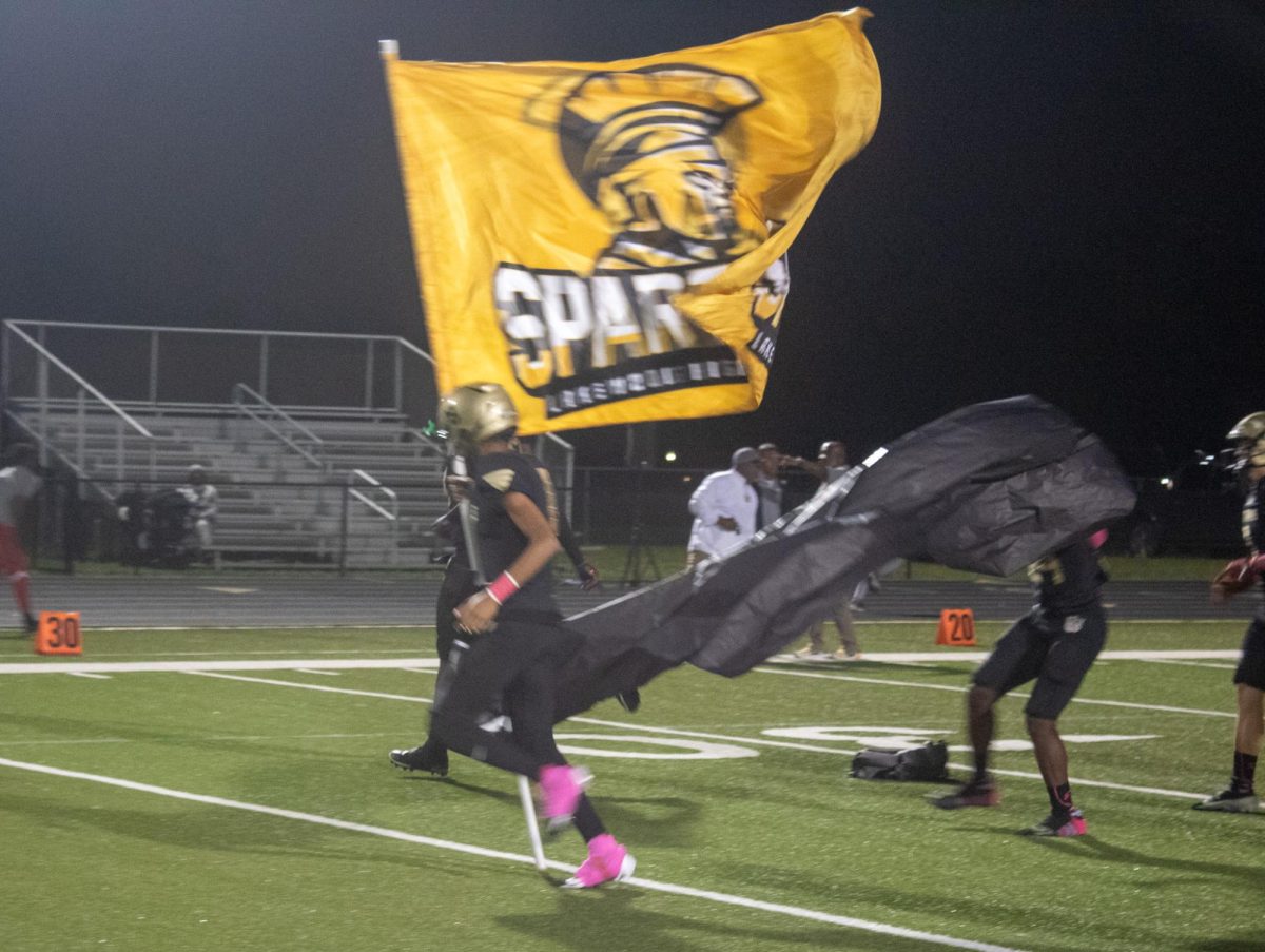 Junior Dmari Roberts carries the Spartan flag down the the football field after a win.