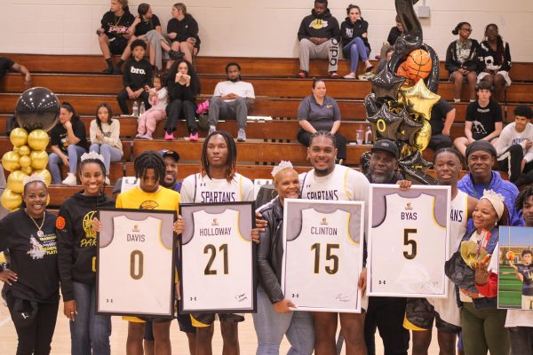 Spartan senior basketball players (from left to right) Elijah Davis, E'Zaveon Holloway, Aiden Clinton, and Keontae Byas hold up framed jerseys on varsity basketball senior night. The frames are signed by the players themselves.