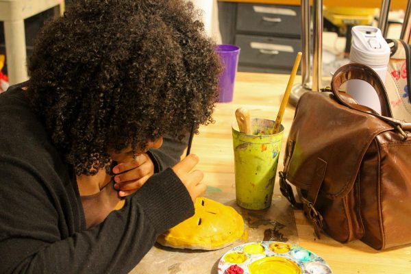 A student paints a clay pie sculpture at Art Club after school.