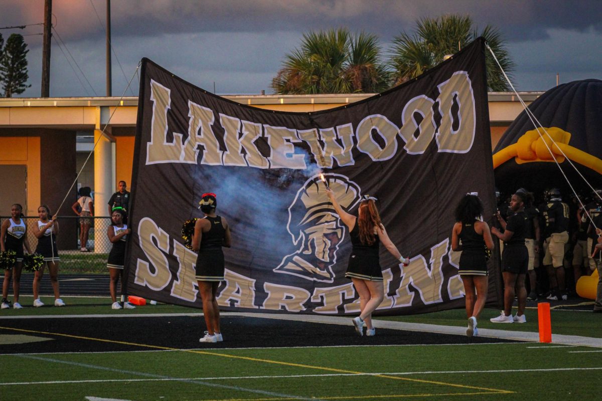 The Lakewood cheer squad sets up the Lakewood flag before the game. The Lakewood football team prepares to run through the flag.