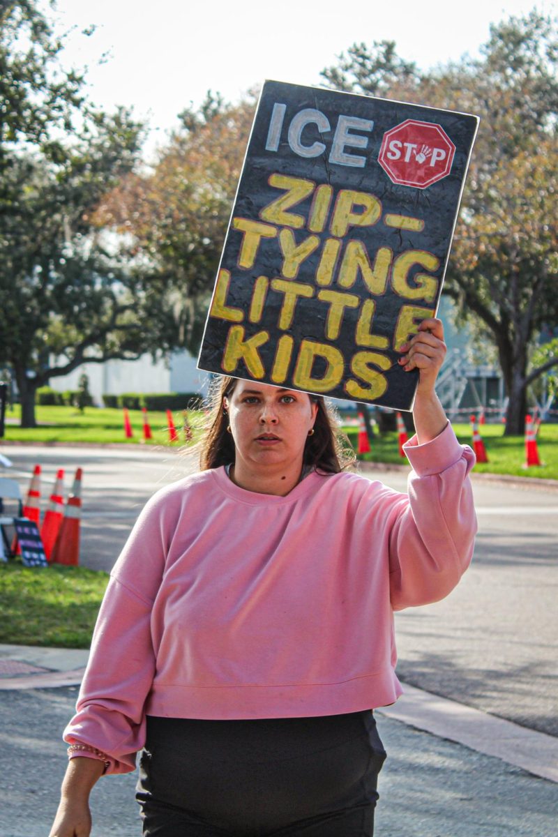 A woman holds a sign as she walks across the street  that reads "ICE Stop Ziptying Little Kids" on Jan 12.